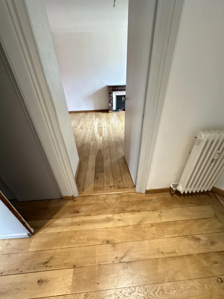 Sol à lames aspect bois, porte et murs peints dans une pièce.