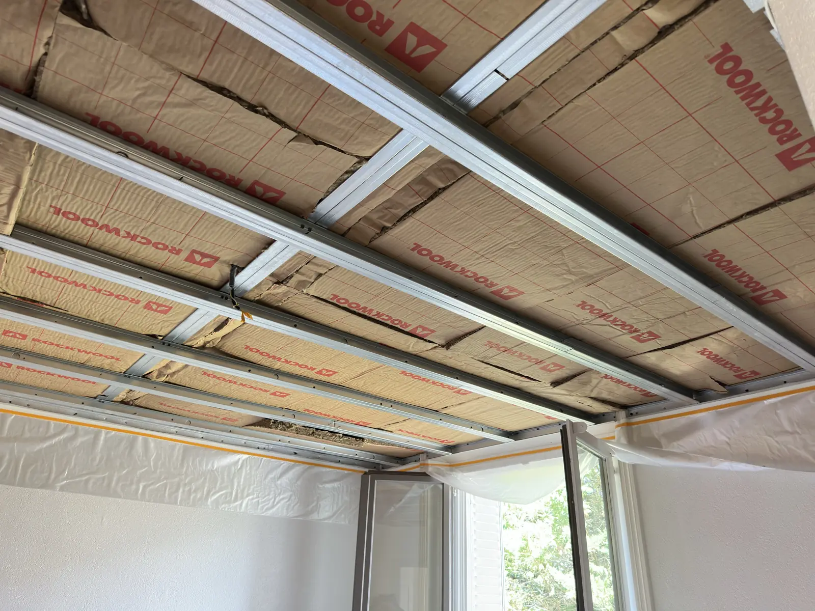 Ossature métallique de plafond avec panneaux de laine isolante visibles.